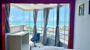 Une chambre avec un lit, un bureau, une chaise et une grande fenêtre donnant sur l’océan.