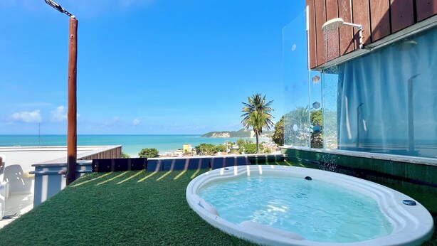 Une piscine sur le toit offrant une vue sur l’océan, entourée d’une terrasse en bois et protégée par une paroi de verre.