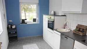 Eine moderne Küche mit weißen Schränken, einem eingebauten Backofen, einer Spülmaschine und einem Fenster mit Blick auf Grünflächen.