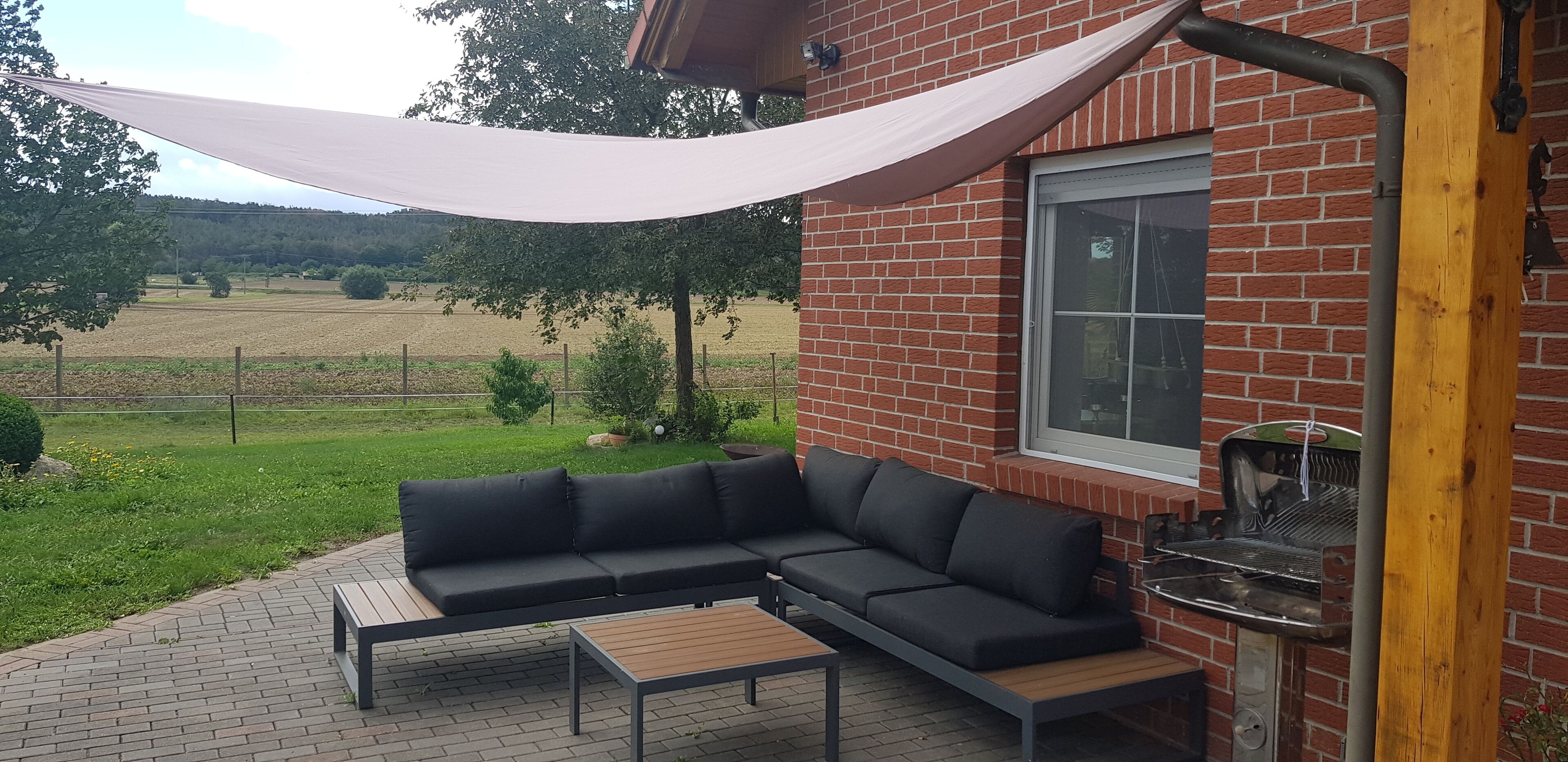 Een terras met een zwarte bank, een houten tafel en een barbecue.