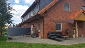 Ein Ziegelhaus mit geneigtem Dach, einer überdachten Terrasse mit Gartenmöbeln und einer großen Leinwand.