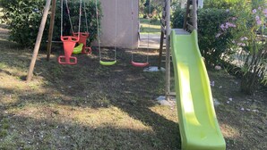 A wooden swing set with a slide, surrounded by greenery and a garden. - Studio 1km from the sea and river (Santa-Maria-Poggio)