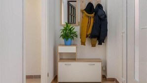 Un pasillo con un banco, una planta en maceta y dos abrigos colgados en la pared.