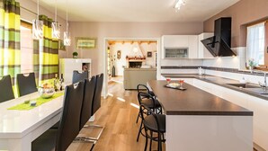 Una cocina moderna con una isla central, armarios blancos y un comedor con una mesa larga y sillas.