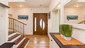 Una escalera conduce a una puerta de madera con un panel de vidrio, un mostrador de recepción con una planta y dos cuadros en las paredes.