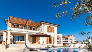 Una casa de dos pisos con piscina, mobiliario exterior y un balcón.