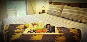 Una cama bien tendida con ropa de cama a rayas, una bandeja con alimentos para el desayuno y una mesita de noche con una lámpara.