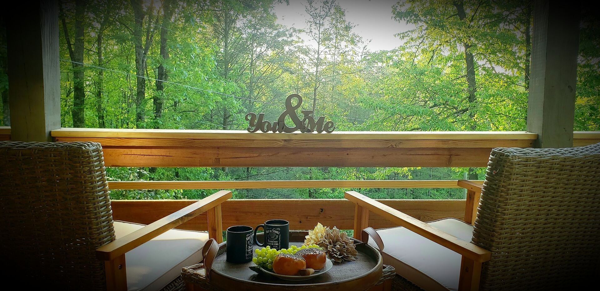 A wooden bench with two wicker chairs, a small table with a plate of food, and a decorative sign with the text 'Get U & Me' in a forested area.