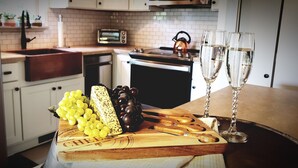 A kitchen with a wooden cutting board holding grapes, cheese, and a cleaver. There are two glasses of champagne on the counter. - Happy Camper 1 Bedroom Cottage by RedAwning (Sevierville)