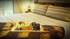 A neatly made bed with striped bedding, a tray with a 'hello' sign, grapes, a bun, and two mugs on a bedspread with a leaf pattern. - Happy Camper 1 Bedroom Cottage by RedAwning (Sevierville)