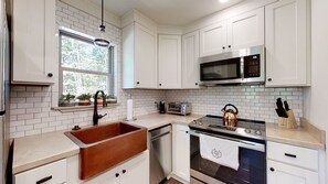 A modern kitchen with white cabinetry, a stainless steel sink, a microwave, a toaster, and a kettle.