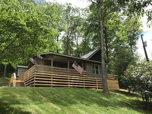 A cabin with a wooden deck, a porch, and an American flag.