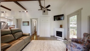 A spacious living room with a leather sofa, a patterned armchair, a fireplace, and a ceiling fan.