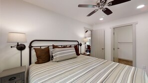A bedroom with a bed, bedside lamps, a ceiling fan, and a door.