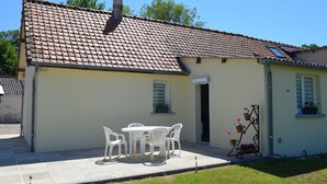 A two-story house with a tiled roof, a small patio with a table and chairs, and potted plants. - Gite Baie de Somme 80  (Pendé)