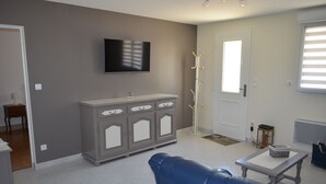 A living room with a grey cabinet, a blue sofa, a small table, and a flat-screen TV mounted on the wall. - Gite Baie de Somme 80  (Pendé)