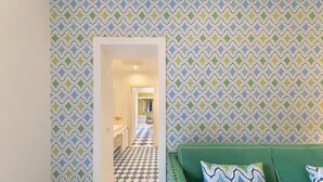 A hallway with patterned wallpaper and a checkered floor leading to a room with a green sofa and patterned cushions. - Luxury Four Bedroom Home (Sorrento)