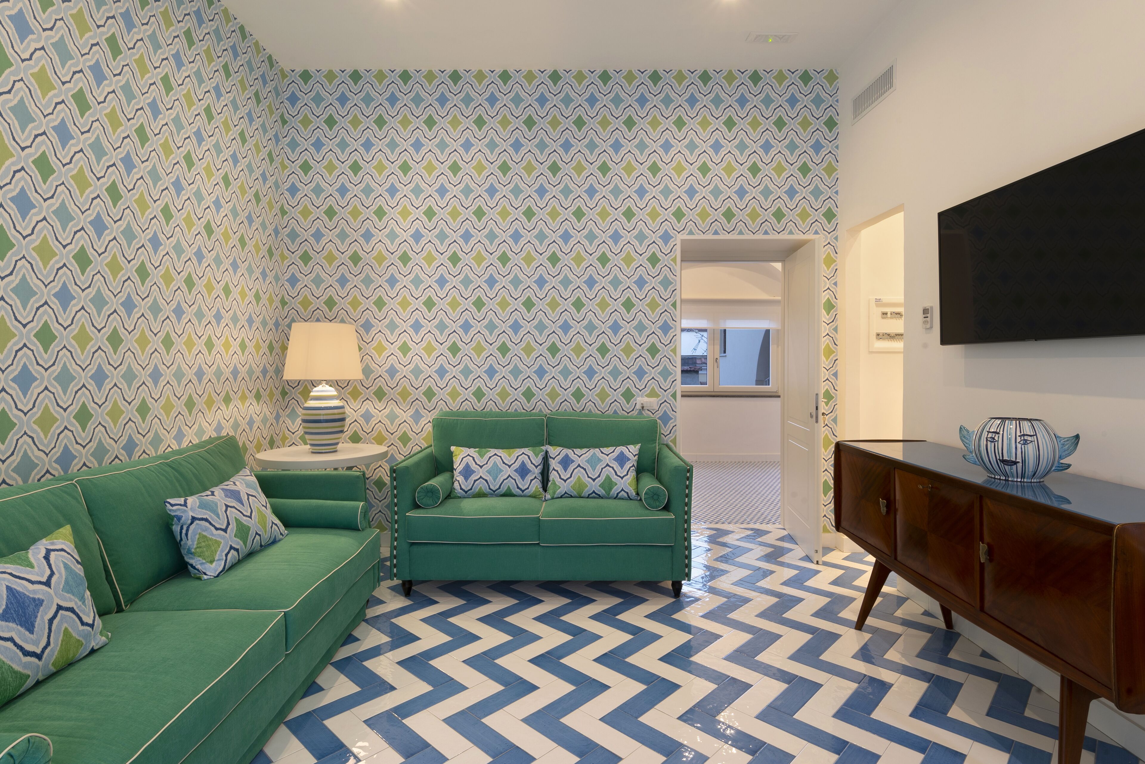 Una sala de estar con un sofá verde, una mesita con una lámpara y un mueble de madera.