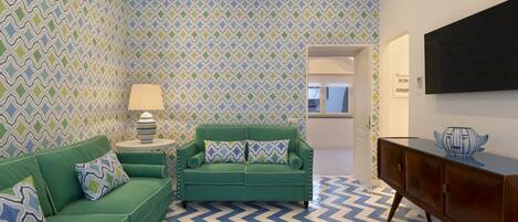 Una sala de estar con un sofá verde, una mesita con una lámpara y un mueble de madera.