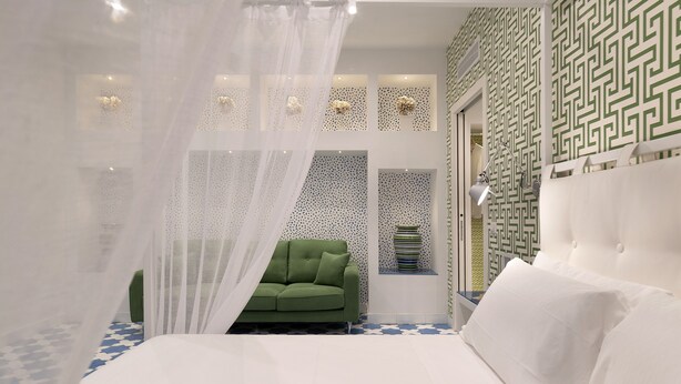 A bedroom with a bed, a green chair, a white canopy, patterned walls, and a window with a decorative item. - Luxury Four Bedroom Home (Sorrento)
