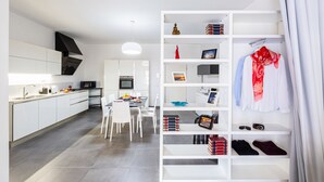 Cocina moderna con muebles blancos, un área de comedor con sillas blancas y una estantería blanca con libros y una bufanda roja.