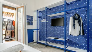 Una habitación de hotel con una cama, un armario azul con un televisor y una ventana con cortinas.