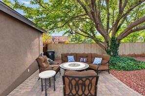 An outdoor patio with a round table, two chairs, and a sofa with cushions.