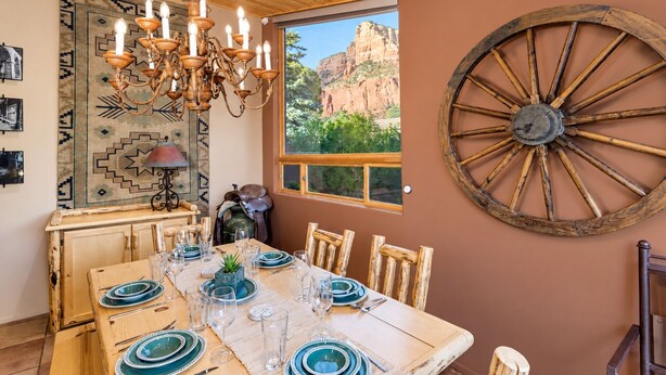 A dining area with a wooden table set for four, a chandelier, and a large wooden wheel decoration on the wall. - Meadow Lark Trail 3BD 2BA W/ Jacuzzi in THE best location (Sedona)