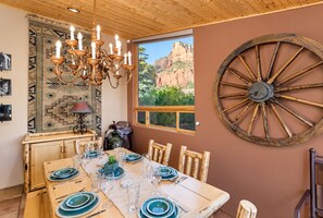 A dining area with a wooden table set for four, a chandelier, and a large wooden wheel decoration on the wall.