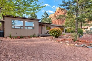 A modern two-story house with a gravel driveway, a small front porch, and a mountain backdrop.