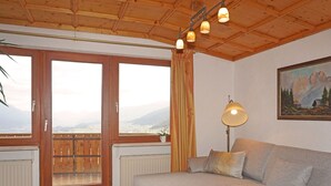 Ein gemütliches Wohnzimmer mit Holzbalkendecke, einem grauen Sofa, einer Stehlampe und einem Gemälde von Bergen.