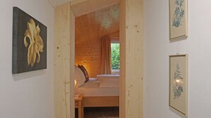 Ein Zimmer in einer Holzhütte mit einem Bett, einem kleinen Tisch und einem Fenster mit Vorhängen.
