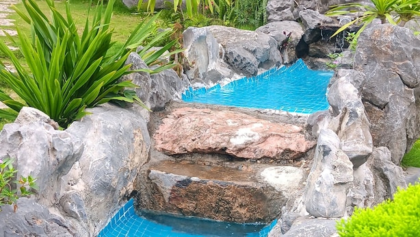 A pool surrounded by rocks and greenery, with a house in the background. - Tran Chau Garden Home (Hai Phong)