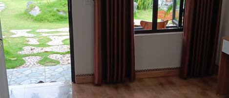 Una habitación con cama, cortinas y vista a un jardín con un edificio de techo rojo.