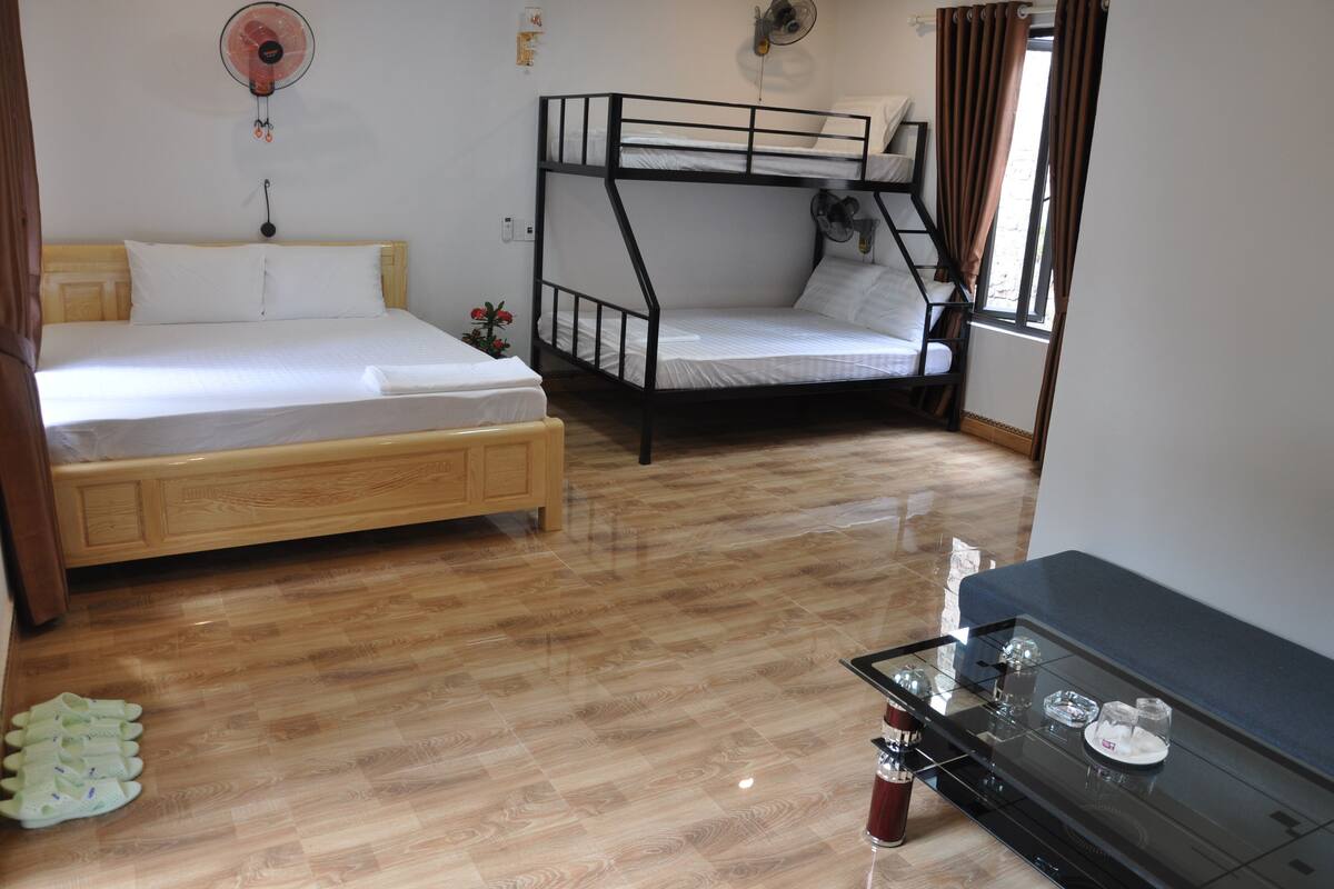 Une pièce avec deux lits superposés, une armoire en bois, une table en verre avec un plateau et un ventilateur fixé au mur.