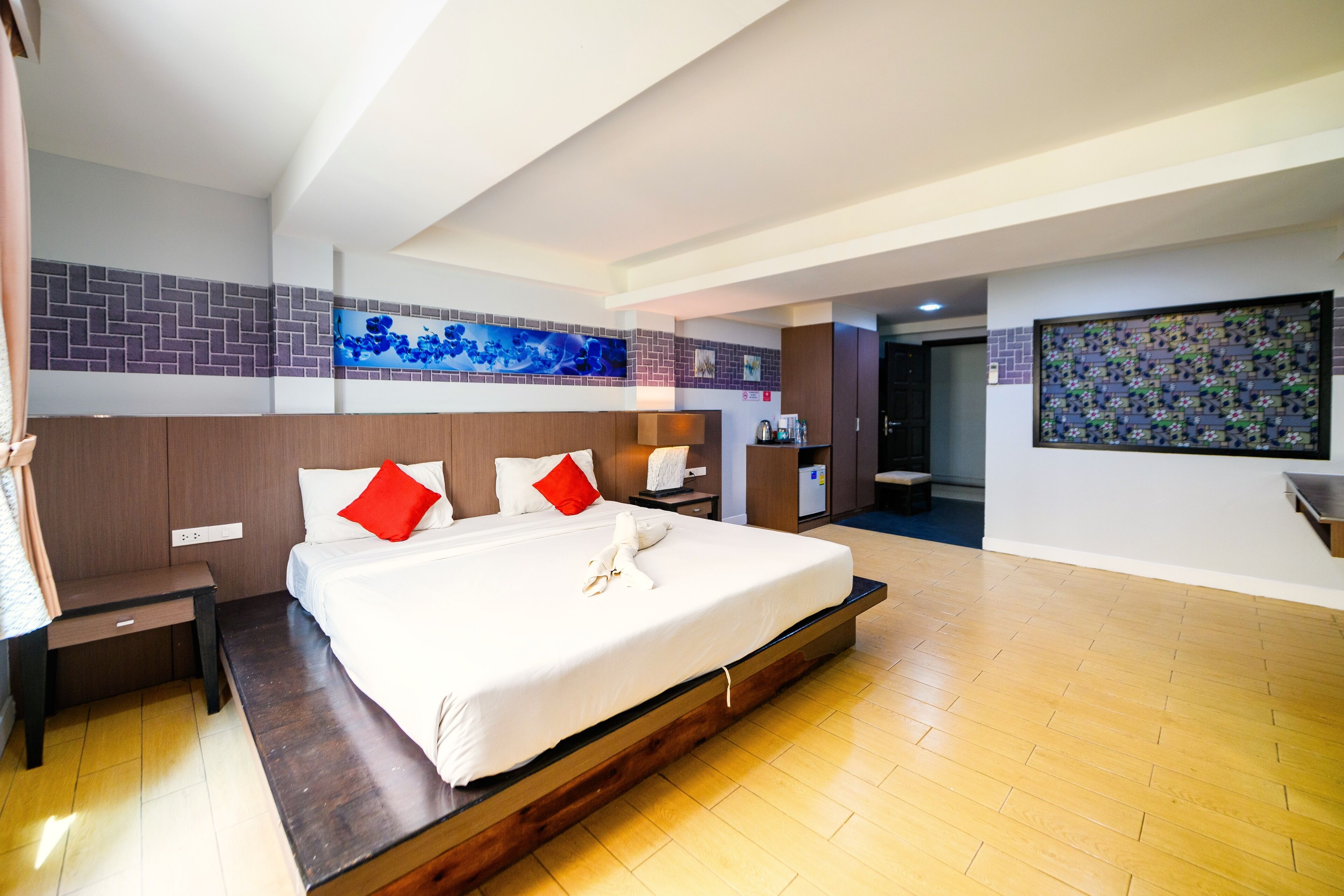 A modern hotel room with a large bed, wooden floor, and a TV mounted on the wall.