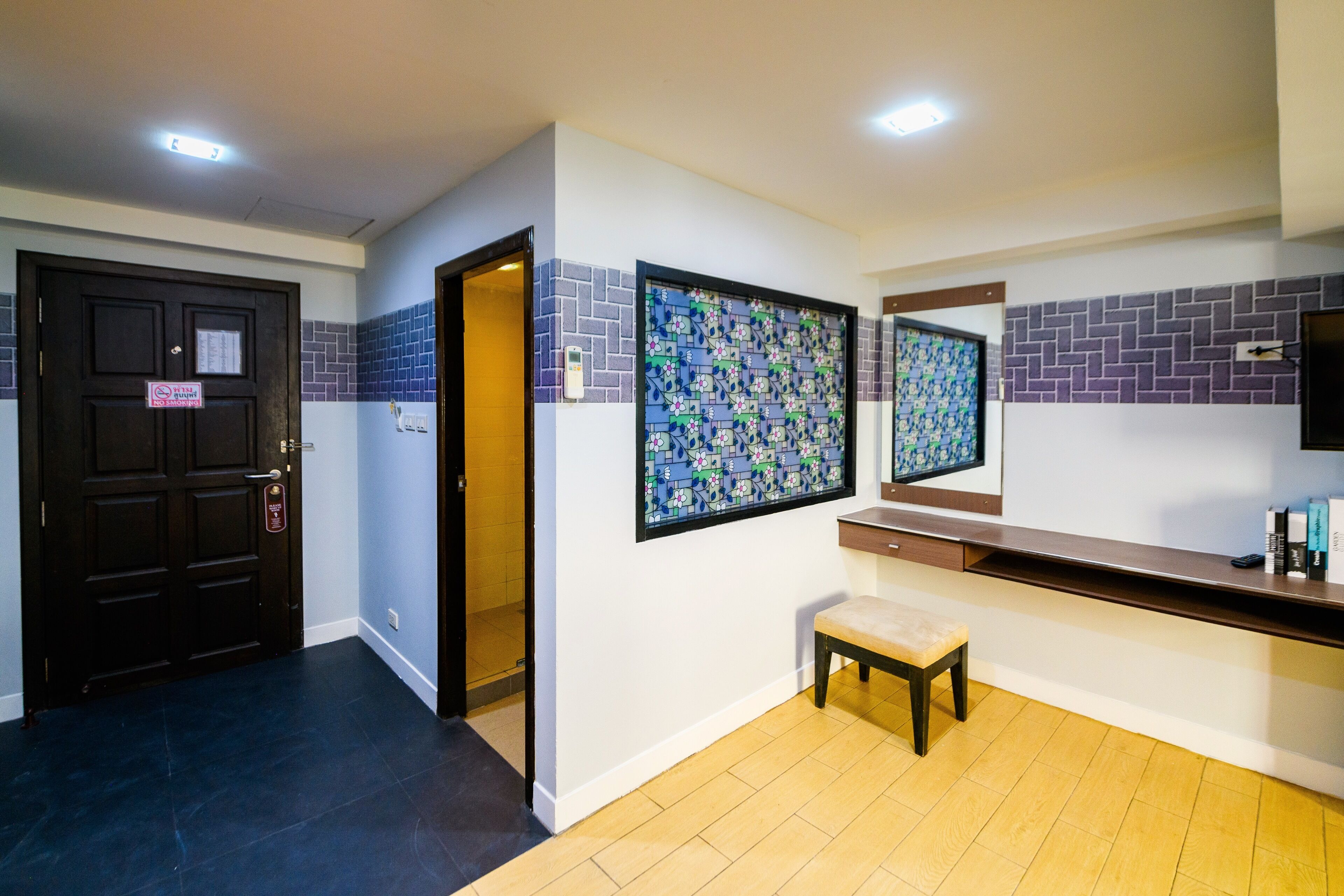 A hotel room with a wooden floor, a bench, a mirror, and a tiled wall with a floral pattern.
