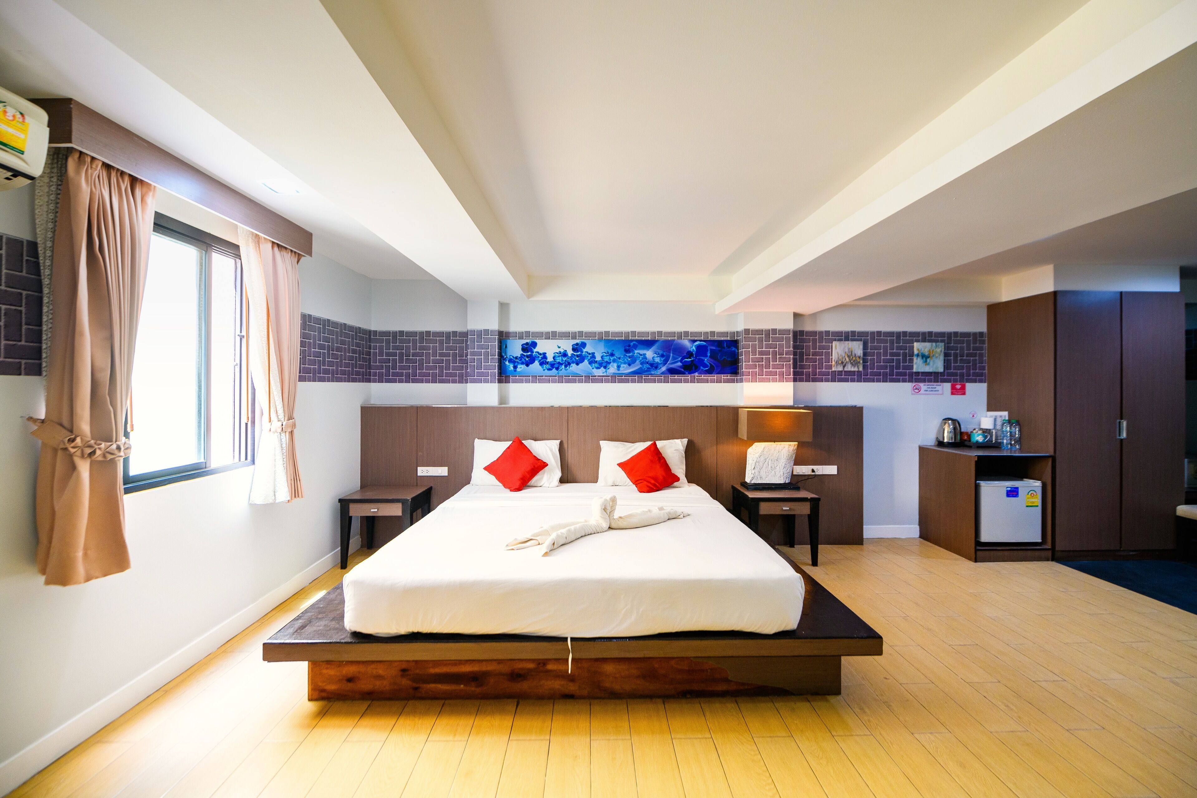A modern hotel room with a large bed, a small kitchenette, and a bathroom visible in the background.