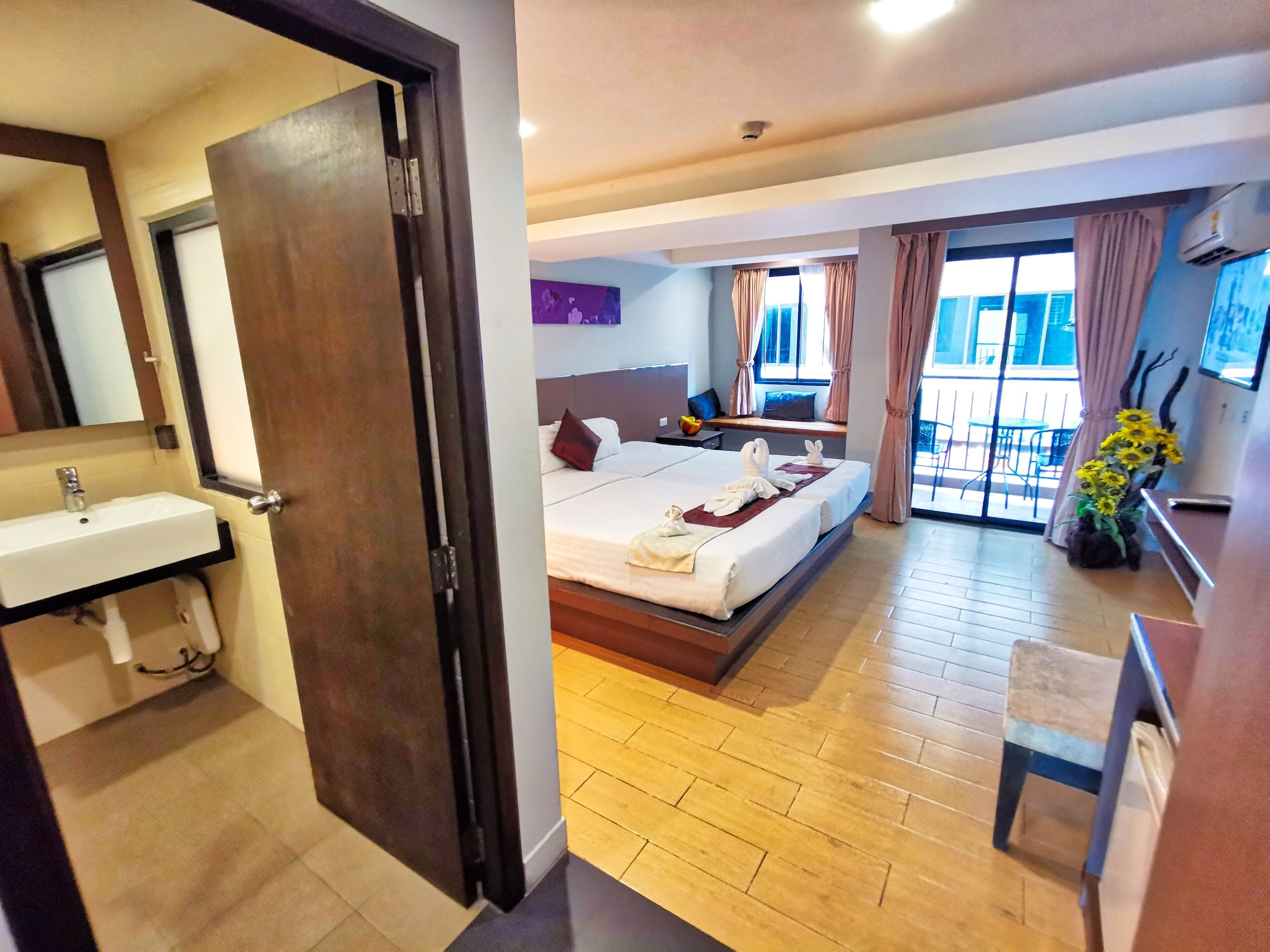 Une chambre d’hôtel avec un lit, une salle de bain avec un lavabo, une grande fenêtre et un balcon avec vue.