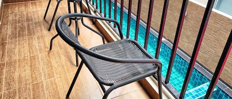 A balcony with a glass table and two wicker chairs, overlooking a swimming pool.