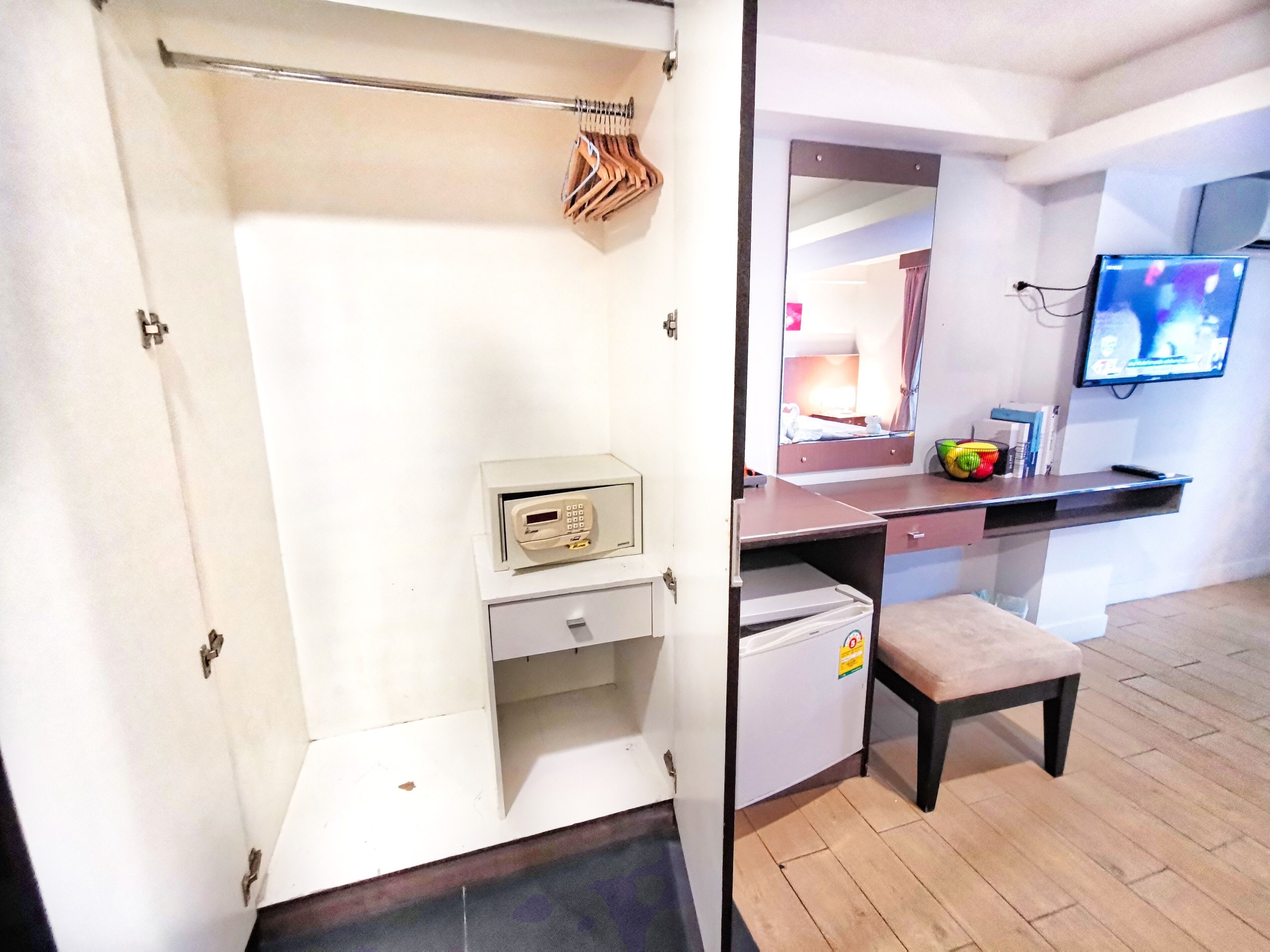 A compact room with a desk, a small refrigerator, a bench, a mirror, and a television.