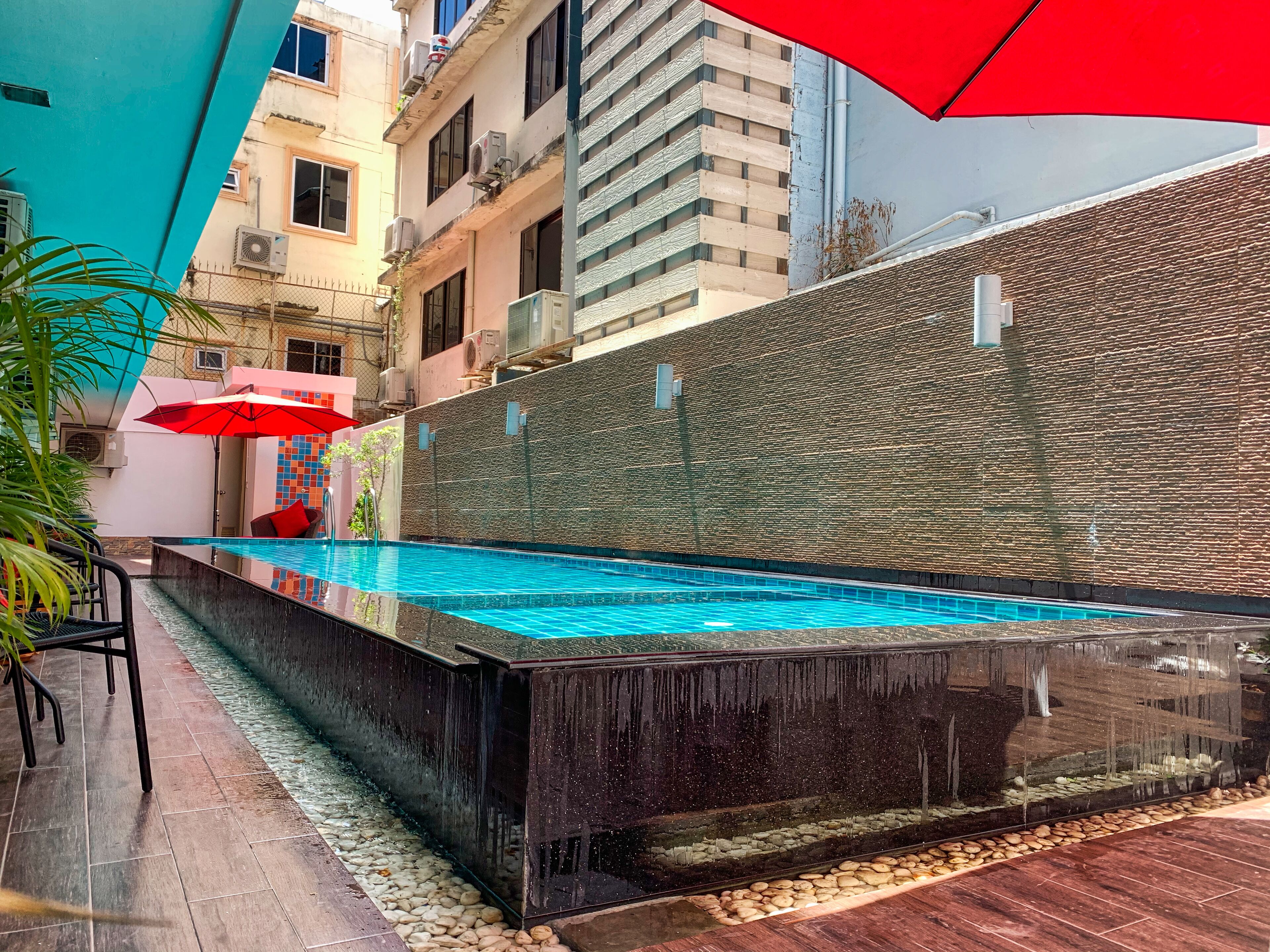 An outdoor swimming pool with a stone wall and a red umbrella.