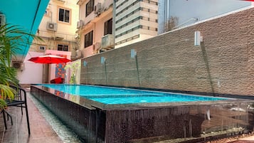 An outdoor swimming pool with a stone wall and a red umbrella.