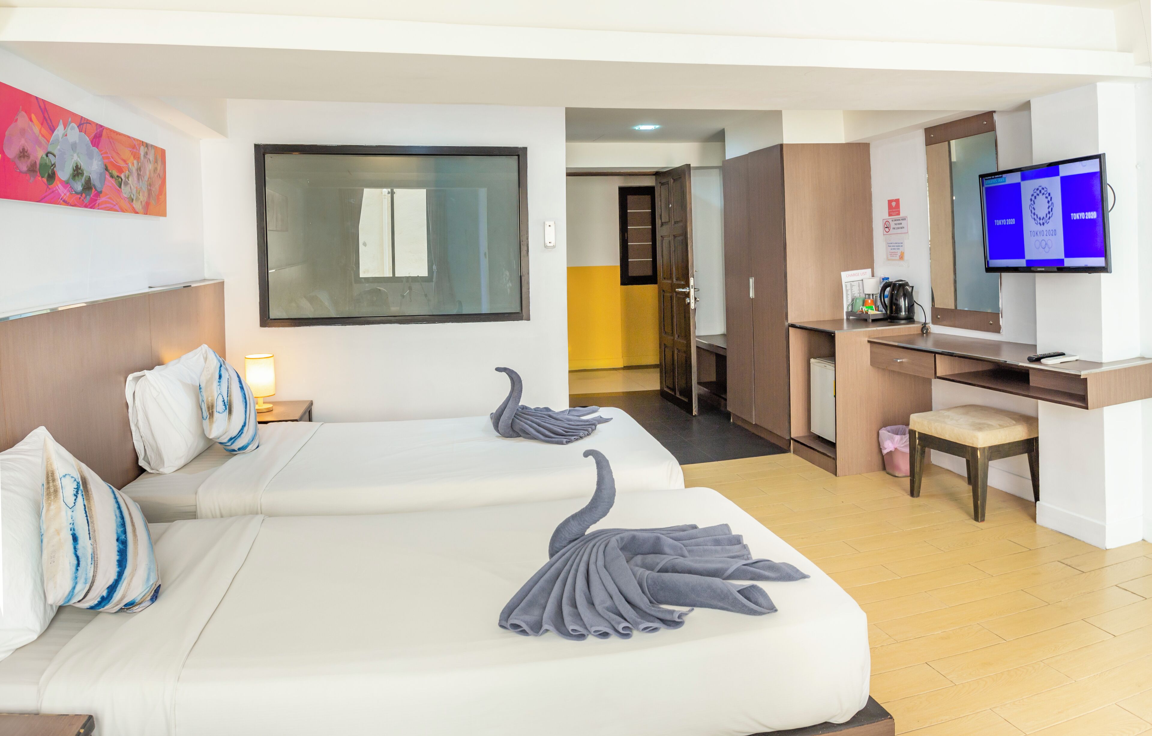A hotel room with two beds, a desk, a TV, and a bathroom visible in the background.