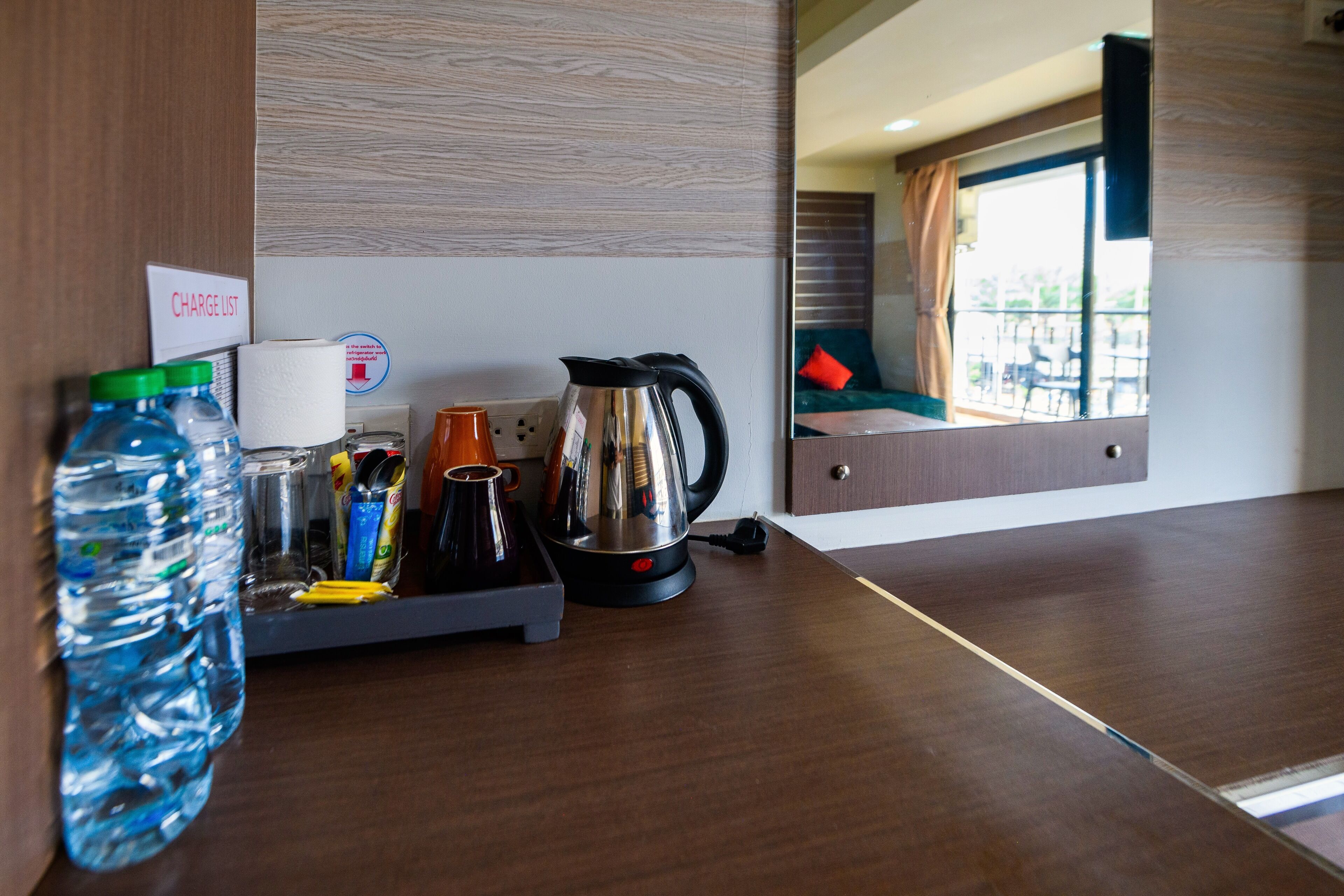 Une chambre d’hôtel équipée d’un comptoir en bois, d’une bouilloire, d’une machine à café, d’une bouteille d’eau et d’une tasse.