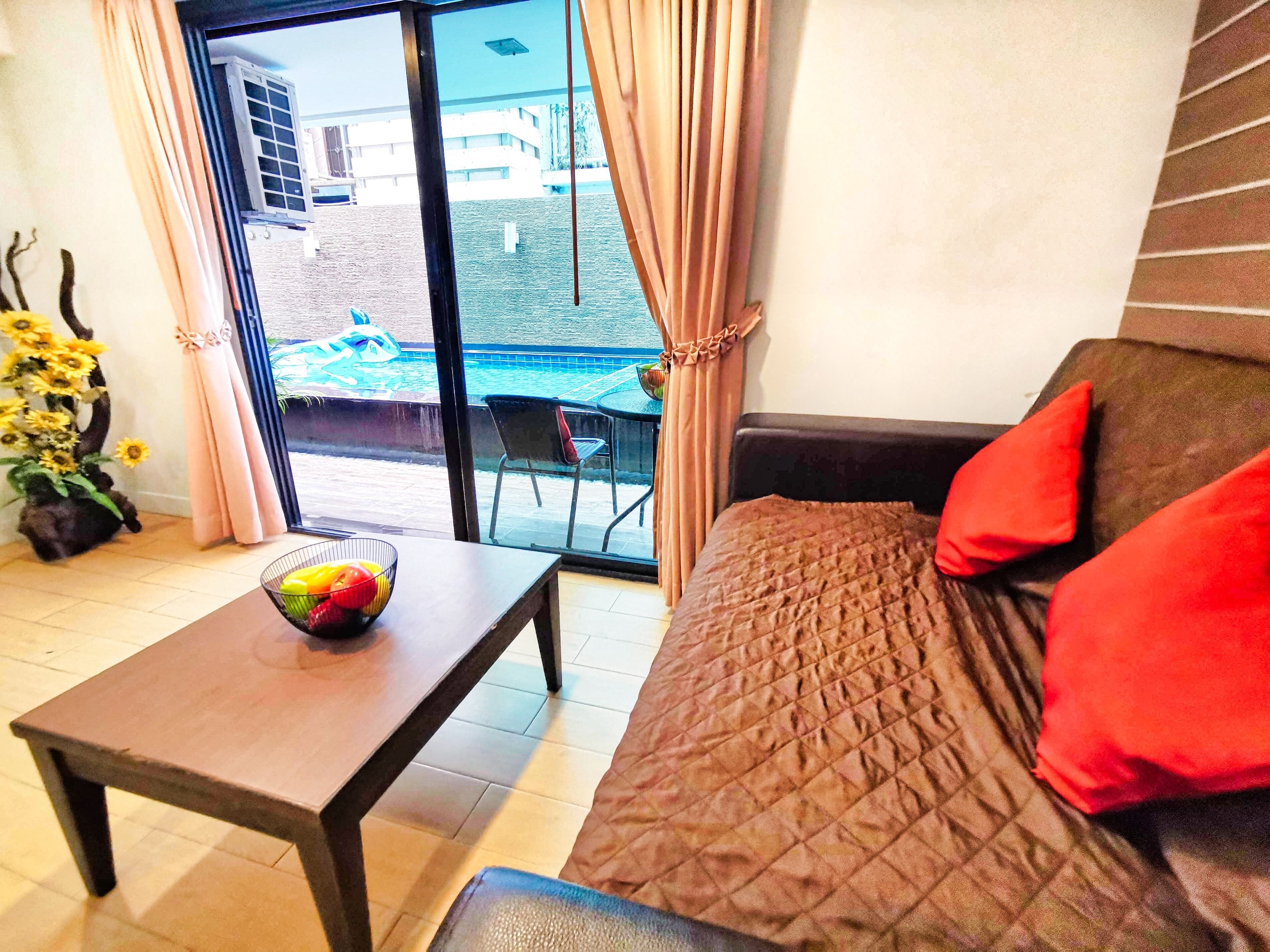 Una habitación con una cama, una mesa con fruta, vista a una piscina y una planta con girasoles.