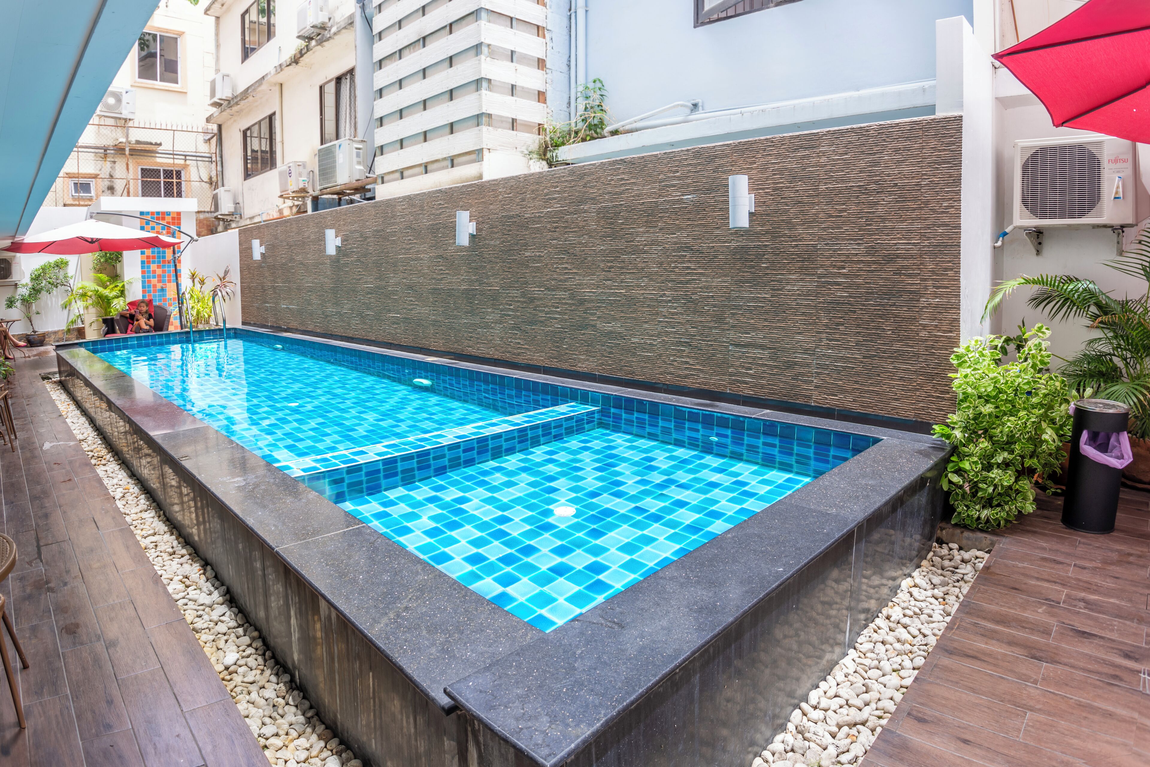 A rectangular outdoor swimming pool with blue tiles, surrounded by a stone wall and wooden deck.