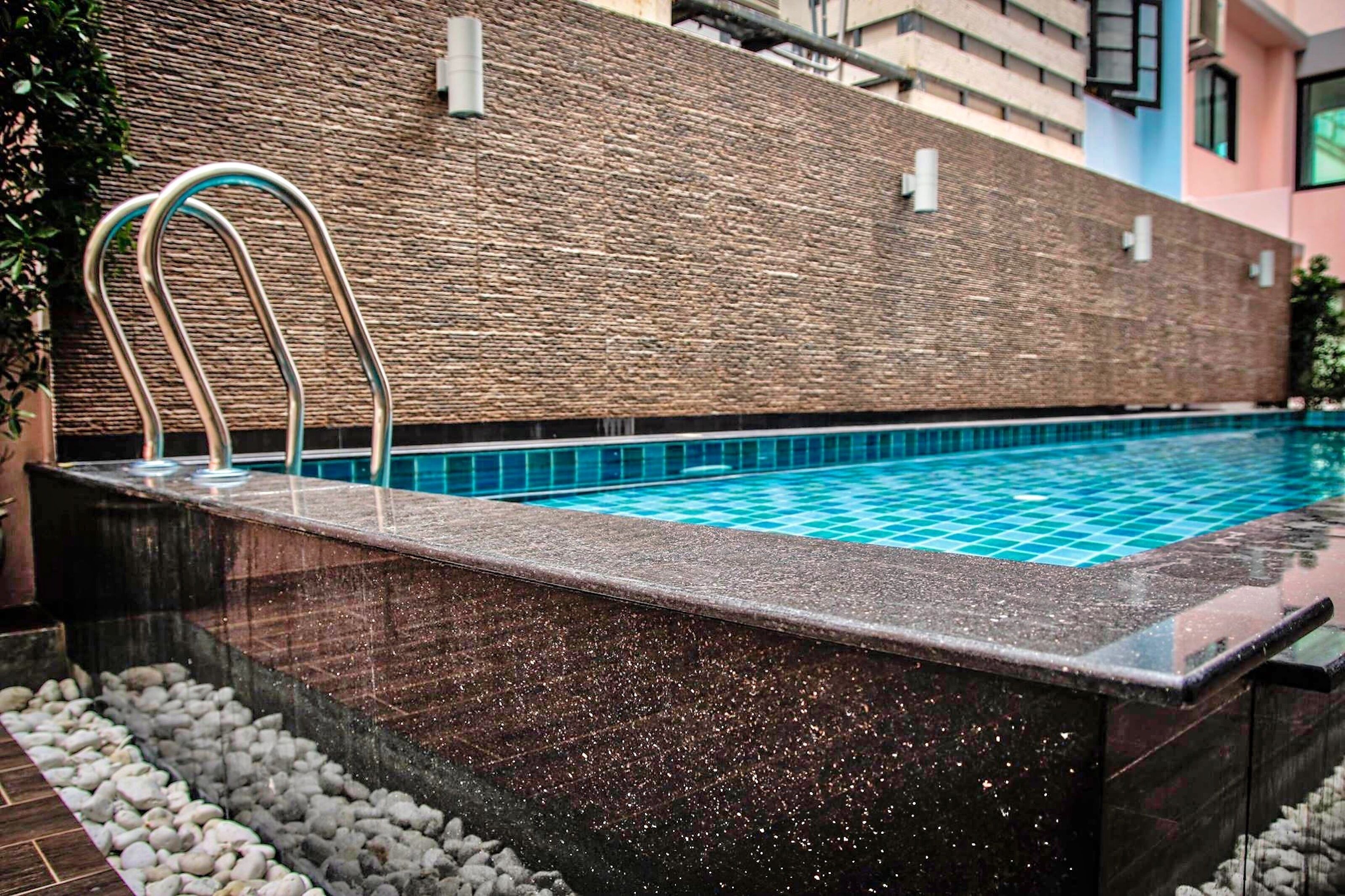A swimming pool with a stone wall and metal handrails.