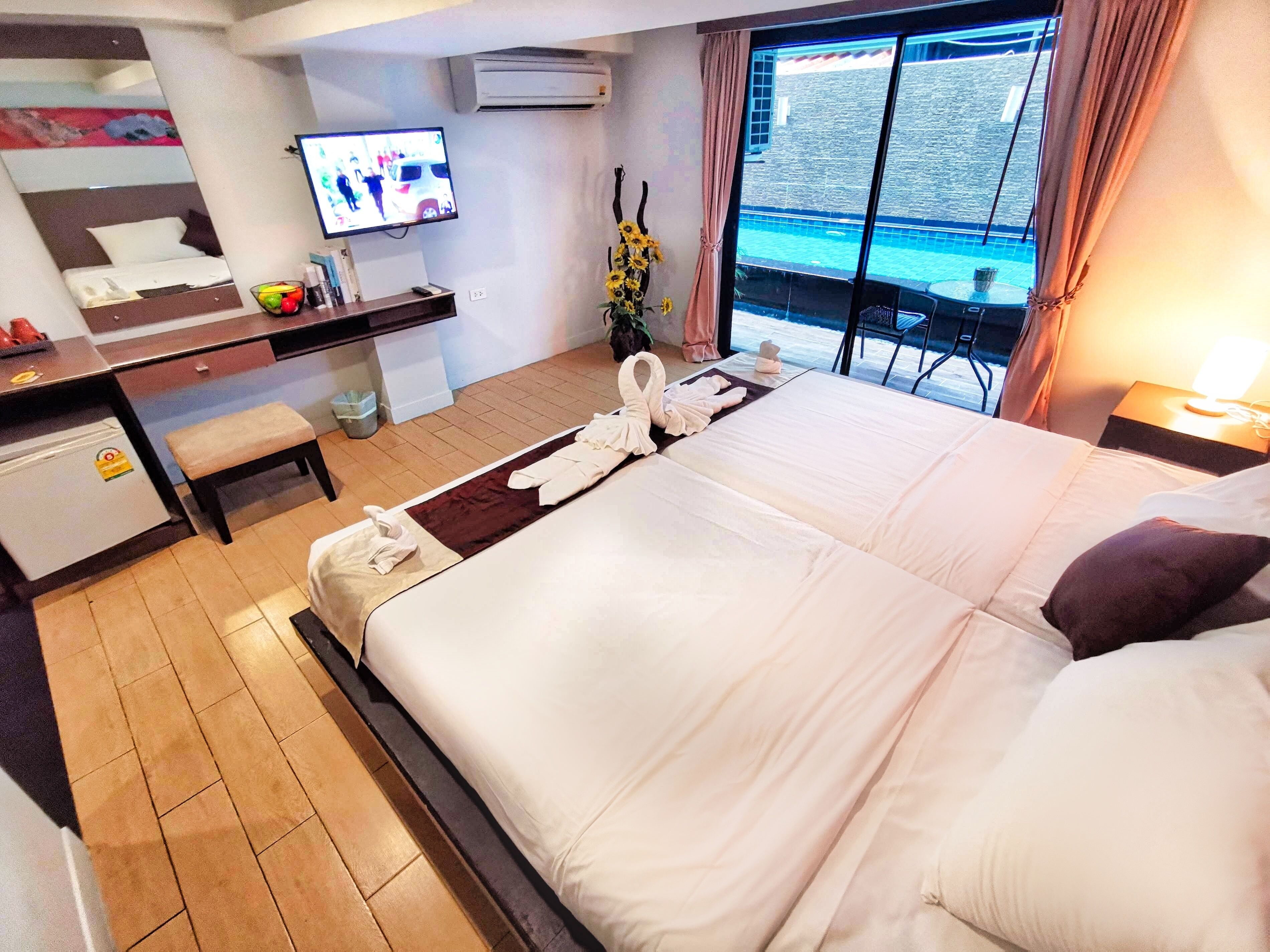 A hotel room with a bed, a desk with a computer, a TV, and a view of a pool.