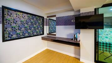 Une pièce avec un plancher en bois, un téléviseur fixé au mur, un bureau avec un miroir et un panneau décoratif mural.
